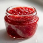 Close-up of a glass jar filled with glistening, bright red strawberry freezer jam, showing visible seeds.