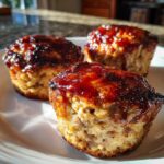 Three perfectly baked mini meatloaf portions topped with a shiny, caramelized glaze served on a white plate.