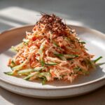A mound of creamy kani salad mixed with shredded cucumber, topped with sesame seeds and chili threads.