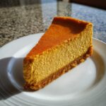 A perfect slice of rich, orange keto pumpkin cheesecake with a graham cracker-style crust on a white plate.