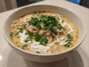 A close-up of a white bowl filled with creamy keto white chicken chili, topped with shredded chicken, sour cream, and fresh cilantro.