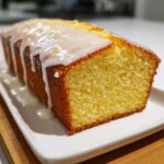 A close-up of a freshly baked lemon pound cake loaf with thick white lemon glaze dripping down the sides.