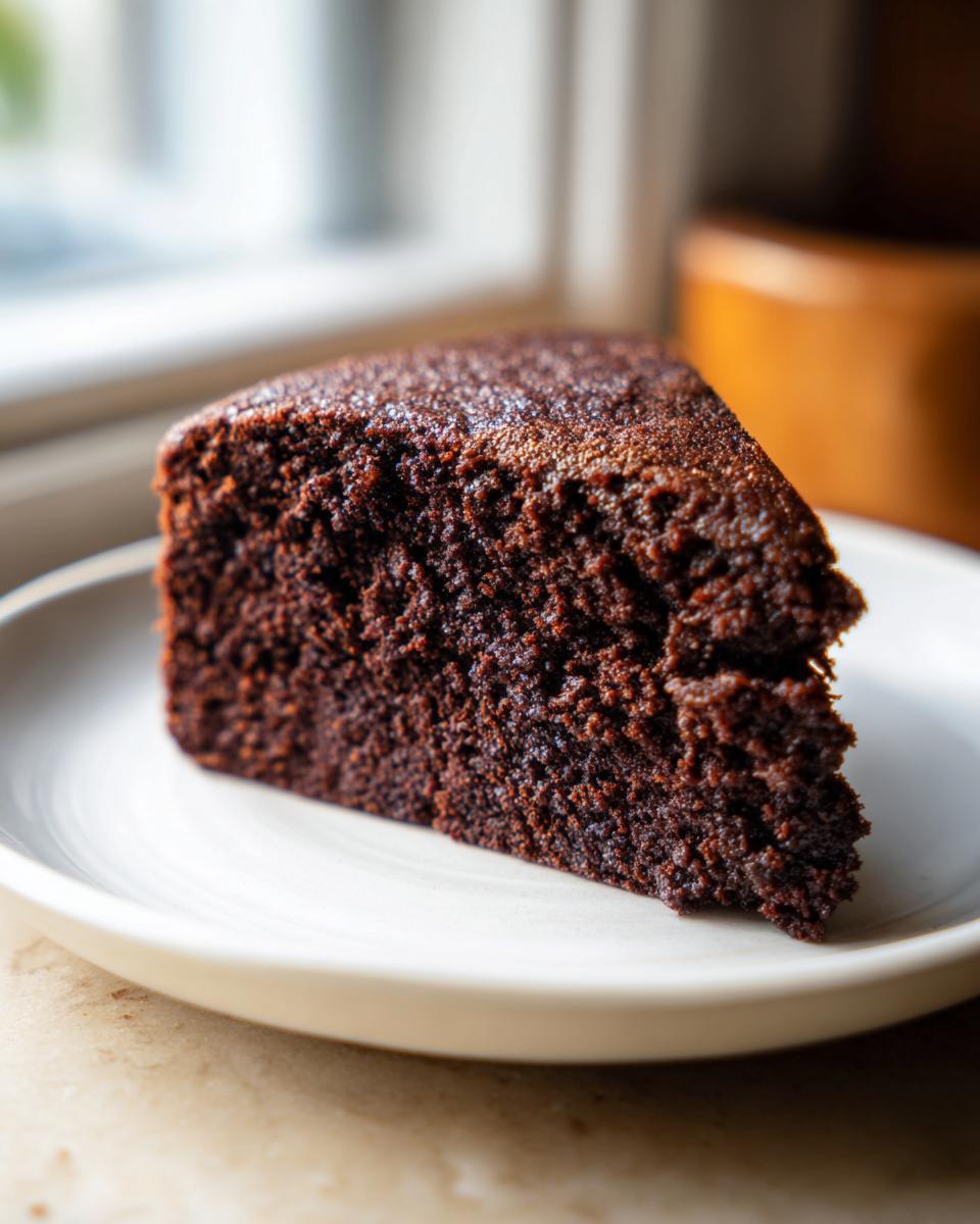 Close-up of a rich, dark slice of moist chocolate cake showing its tender, crumbly texture on a white plate.