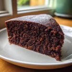 Close-up of a single slice of moist chocolate cake on a white plate, highlighting its rich, dark crumb.