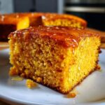 Close-up of a moist, orange slice of sweet potato cornbread topped with dripping honey on a white plate.