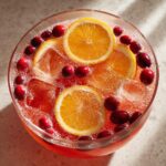Overhead view of a vibrant non-alcoholic Christmas punch garnished with orange slices and fresh cranberries.