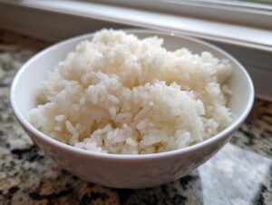 Close-up of a white bowl filled with perfectly cooked, glossy sushi rice.