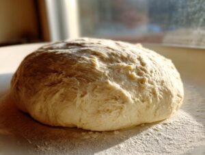 A freshly kneaded ball of pizza dough resting on a lightly floured surface, ready for the amazing pizza dough recipe.