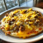 Close-up of a freshly baked sausage gravy breakfast pizza topped with scrambled eggs and melted cheese.