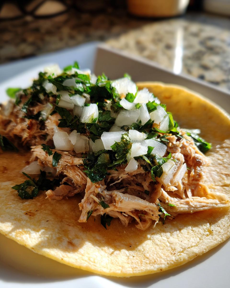 A close-up shot of a single, delicious chicken tacos served on a corn tortilla, topped with shredded chicken, diced white onion, and fresh cilantro.