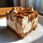 A perfect square slice of no-bake biscoff cheesecake with a graham cracker crust, topped with caramel swirls.