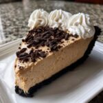 A decadent slice of peanut butter pie with a dark chocolate crust, topped with crushed cookies and whipped cream rosettes.