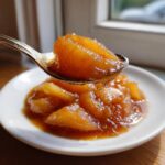 A spoonful of thick, caramelized apple pie filling, rich with cinnamon, being lifted from a small white plate.