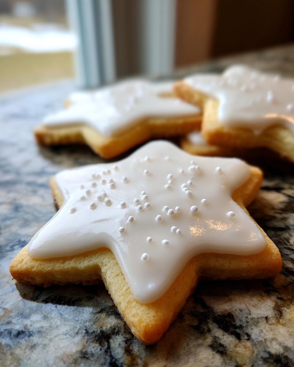 Close-up of a star-shaped sugar cookie topped with smooth white cookie icing recipe and white nonpareils.