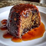 Close-up of a single serving of sticky toffee pudding recipe, drenched in rich toffee sauce.
