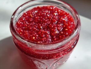 Close-up view of vibrant red strawberry freezer jam, showing visible seeds, inside a clear glass jar.