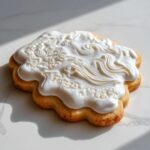 Close-up of a scalloped sugar cookie topped with thick, glossy white sugar cookie icing piped in decorative swirls.