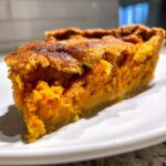 Close-up of a thick slice of sweet potato cobbler showing the vibrant orange filling and flaky crust.