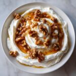 Overhead view of creamy whipped ricotta dip swirled in a white bowl, topped with honey and candied walnuts.