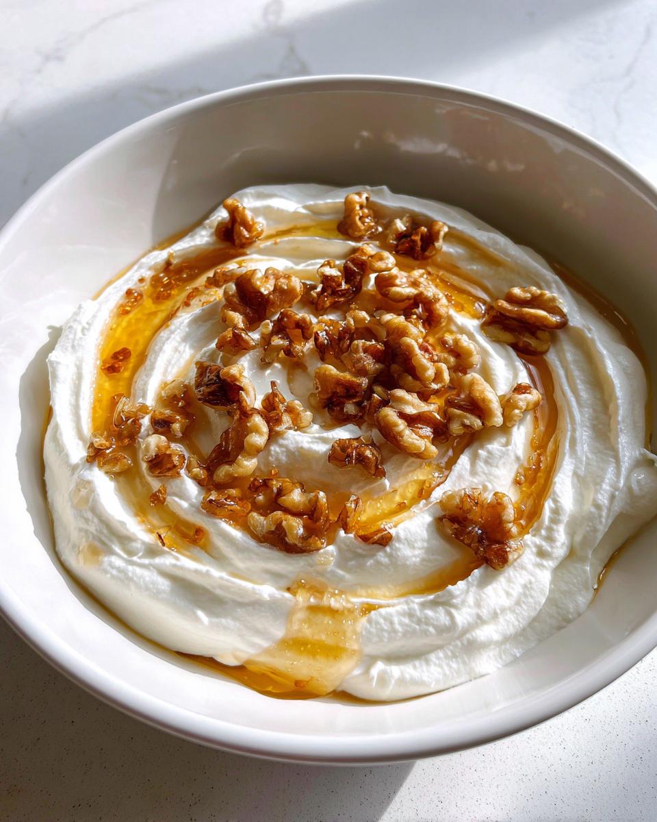 Close-up of a bowl of whipped ricotta dip with hot honey drizzled over it and topped with walnuts.