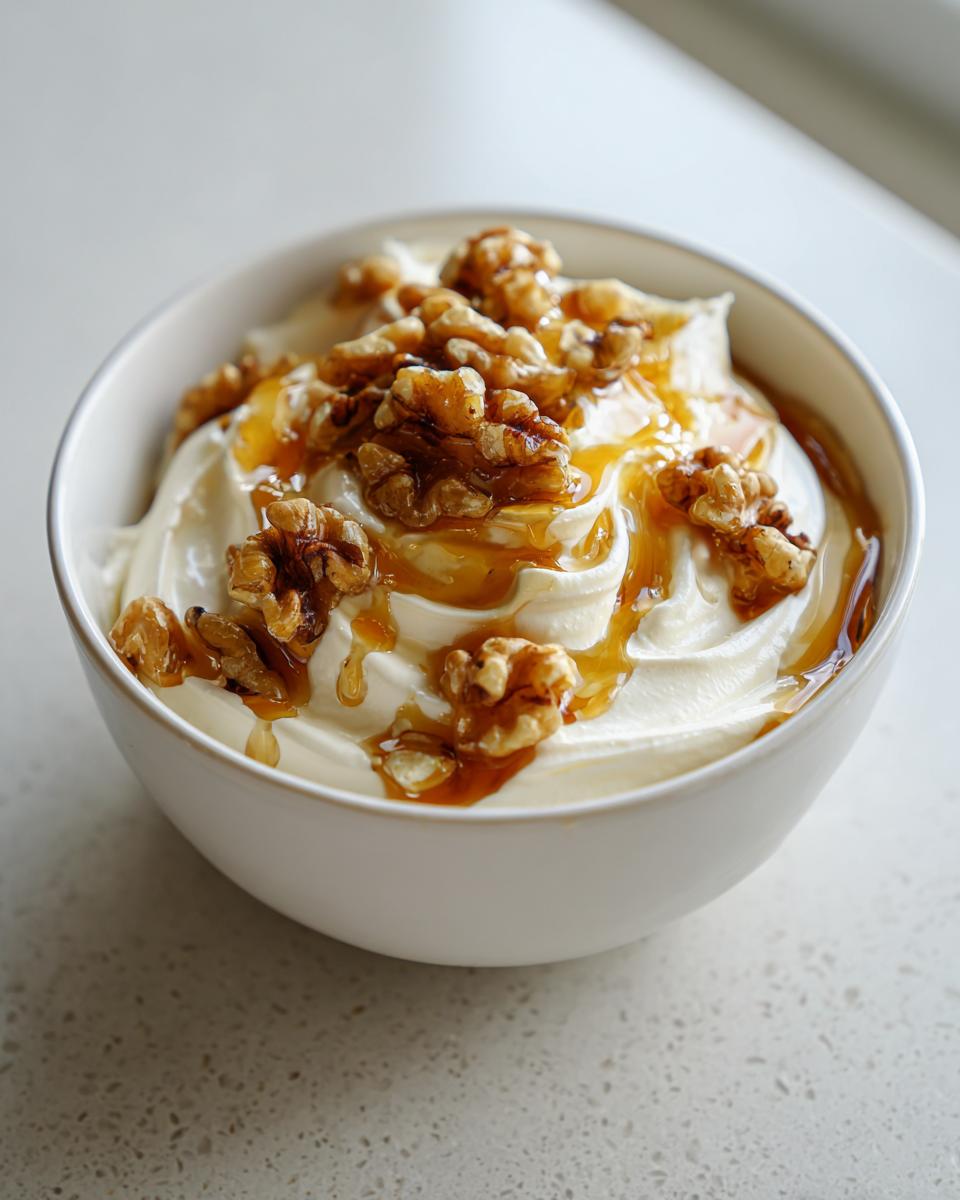 Close-up of a white bowl filled with whipped ricotta dip topped with walnuts and drizzled with hot honey.