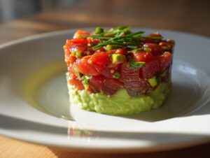 A beautifully plated, cylindrical serving of tuna tartare layered over mashed avocado, garnished with chives.