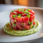 Close-up of vibrant red tuna tartare stacked neatly on a bed of creamy green avocado puree.