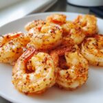 Close-up of perfectly cooked air fryer frozen shrimp, seasoned with spices, piled on a white plate.