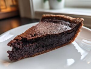 Close-up of a rich, dark slice of fudge pie resting on a white plate.