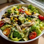 A vibrant bowl of southwest salad featuring shredded chicken, avocado, corn, black beans, tomatoes, and creamy dressing.