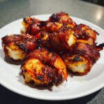 Close-up of several perfectly cooked bacon wrapped shrimp with crispy, caramelized bacon served on a white plate.