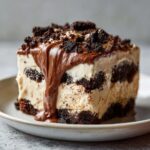 A decadent square serving of Baileys Chocolate Cheesecake Trifle layered with cream and dark cookie crumbs, topped with chocolate fudge.