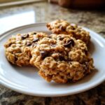 Three freshly baked banana oatmeal cookies loaded with chocolate chips resting on a white plate.