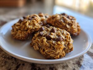 Four freshly baked banana oatmeal cookies studded with chocolate chips resting on a white plate.