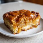 A close-up of a square slice of caramel apple dump cake with gooey caramel topping and soft cake base.
