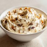 A close-up of rich, creamy caramelized onion dip swirled in a white bowl, featuring visible pieces of caramelized onion.