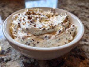 Close-up of creamy caramelized onion dip swirled in a white bowl, featuring visible bits of dark caramelized onions.