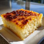 A square slice of moist cassava cake with a beautifully caramelized, glossy brown top, served on a white plate.