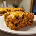 Close-up of a square serving of Mexican rice casserole topped with melted cheddar cheese, black beans, and corn.