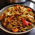 Close-up of a bowl filled with savory chicken chow mein recipe, featuring noodles, chicken pieces, carrots, and cabbage.