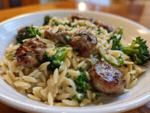 A close-up view of a creamy bowl of chicken sausage and broccoli orzo, featuring browned sausage pieces and bright green florets.