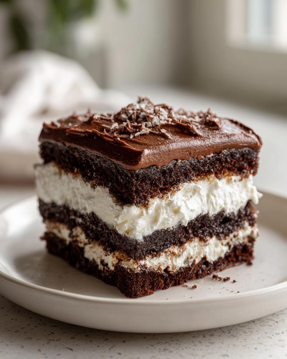 A square slice of layered chocolate italian love cake with white cream filling and chocolate frosting.