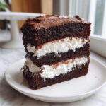 A tall, decadent slice of dark chocolate cake layered with thick white cream filling and topped with chocolate frosting, resembling an italian love cake.