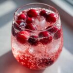 Close-up of a bubbly, pink champagne punch garnished with whole cranberries and ice cubes.