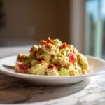 Close-up of a creamy blt chicken salad featuring chunks of chicken, avocado, tomatoes, and crispy bacon bits served on a white plate.