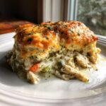 A close-up serving of creamy chicken cobbler featuring shredded chicken, vegetables, and a thick, golden, cheesy biscuit topping.