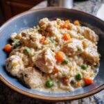 Close-up of creamy one pot chicken and rice mixed with peas and carrots, served in a rustic blue bowl.