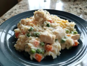 A close-up serving of creamy one pot chicken and rice mixed with peas and carrots on a dark blue plate.