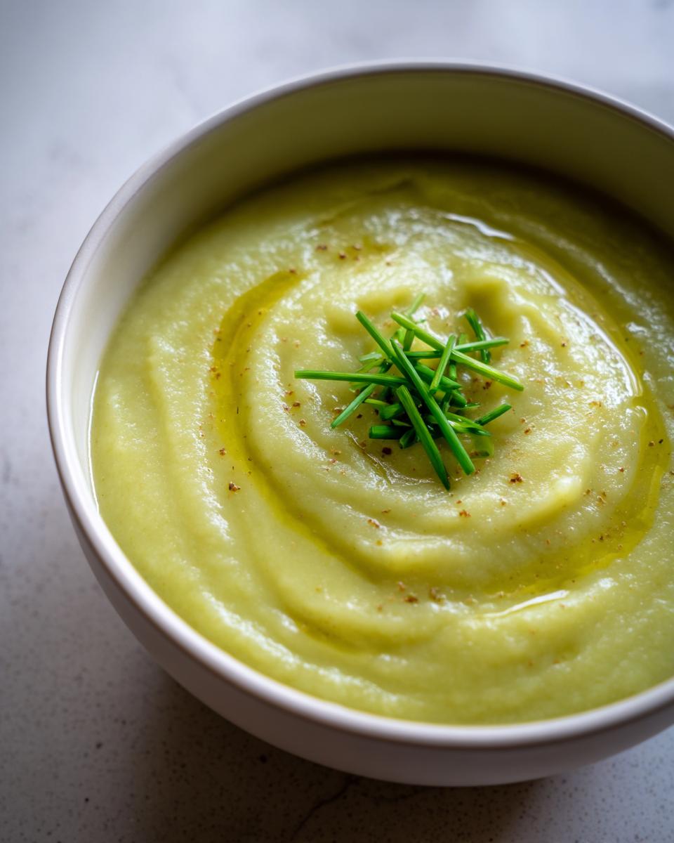 Close-up of a bowl of smooth, creamy potato leek soup garnished with fresh chives and a swirl of olive oil.