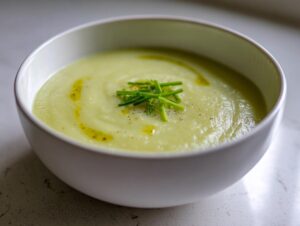 Close-up of a bowl of smooth, creamy potato leek soup garnished with fresh chives and a drizzle of olive oil.